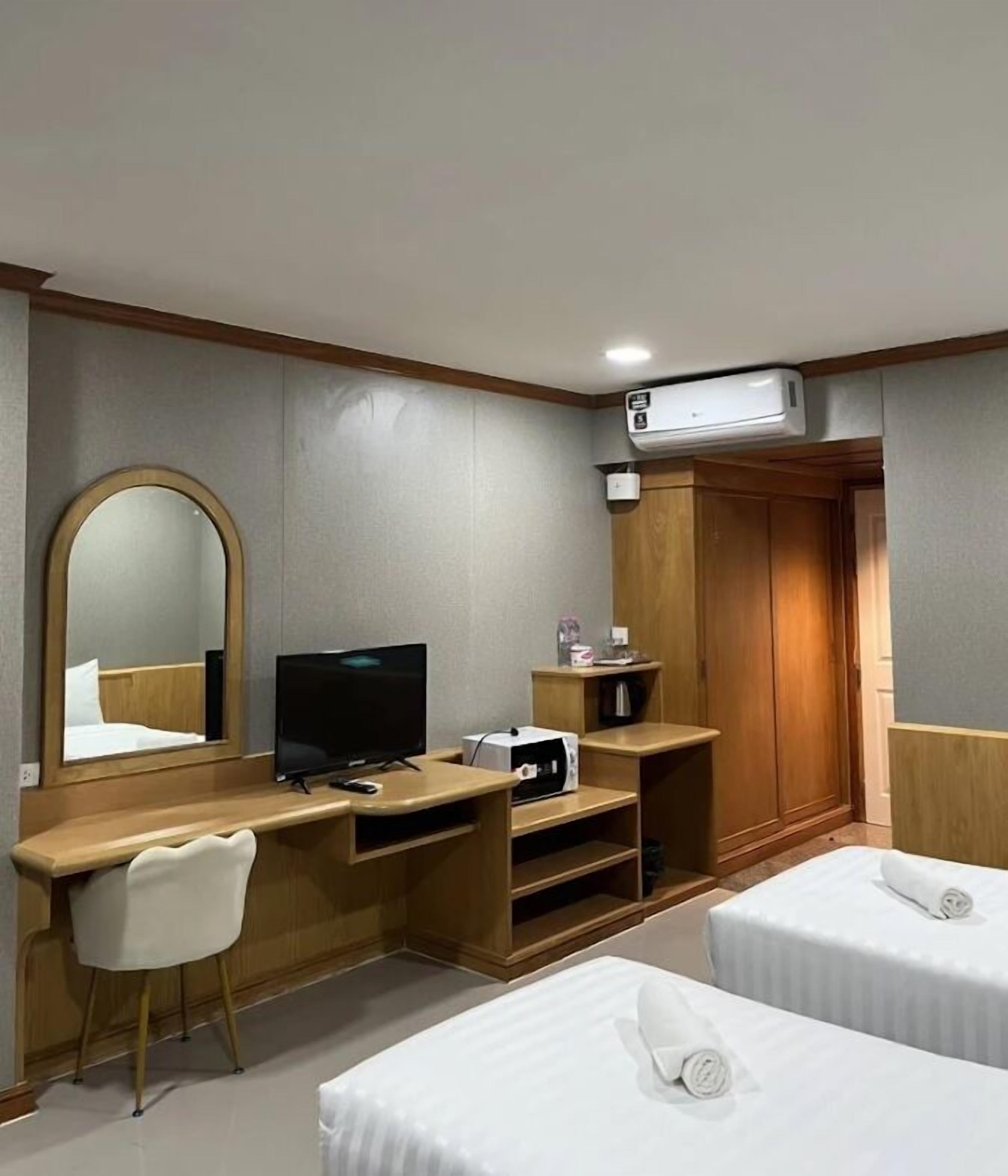A hotel room with a wooden desk, a television, a mirror, a wardrobe, and two beds.