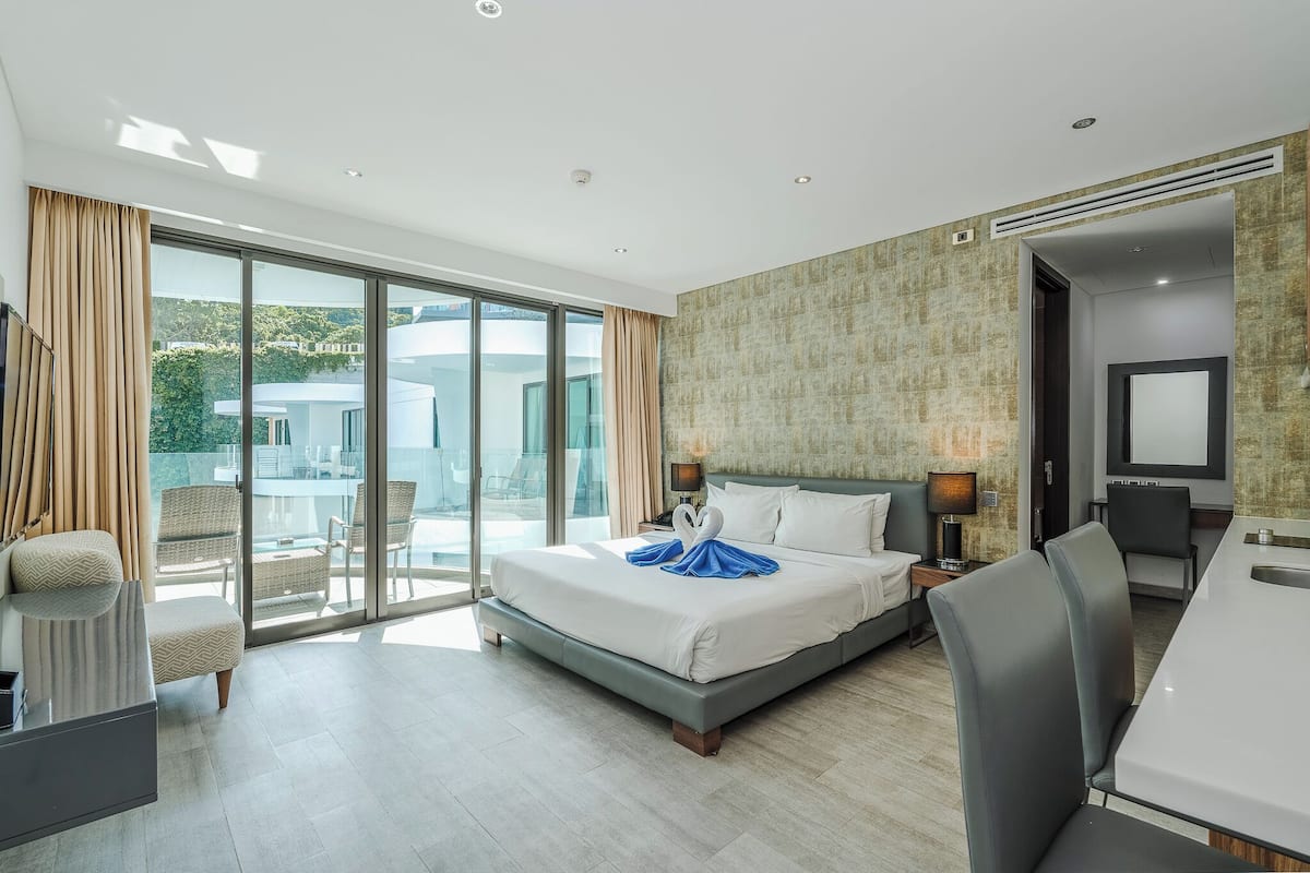 A modern hotel room with a large bed, a desk, and a balcony with a view.