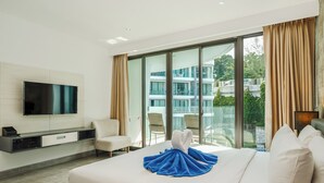 Et hotelværelse med en stor seng, et fladskærms-tv, et siddeområde med stole og en balkon med udsigt til bygninger.
