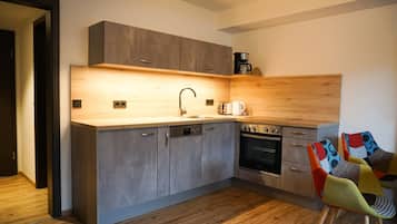 A modern kitchen with grey cabinets, a wooden countertop, a coffee machine, and a colorful chair.