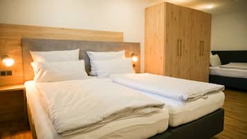 A modern hotel room with a large bed, a wooden wardrobe, and a nightstand with a lamp.