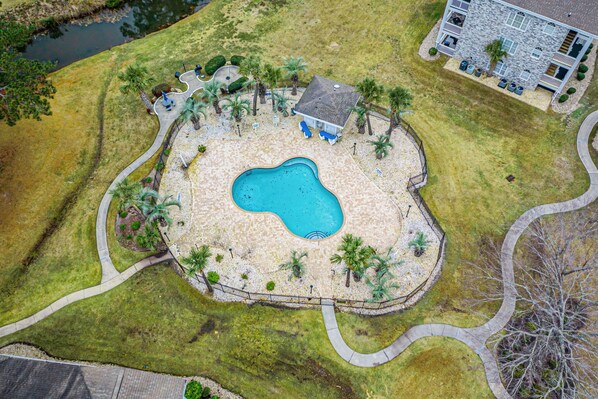 An aerial view of a residential property with a swimming pool, palm trees, and a house.