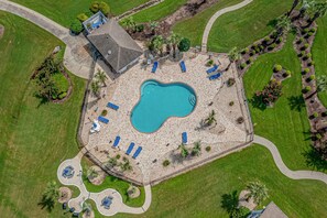 An aerial view of a property with a swimming pool, lounge chairs, and a small building.