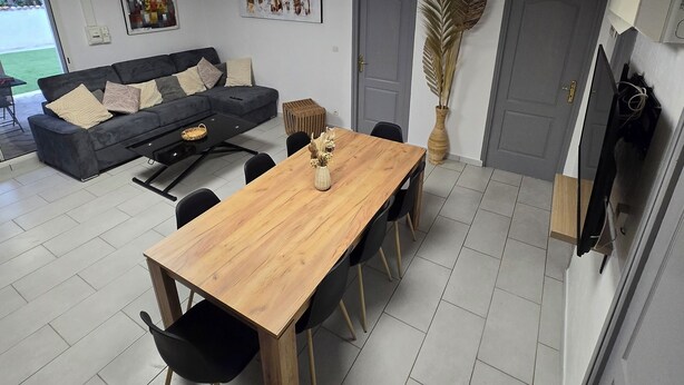 A modern living room with a wooden dining table, black chairs, a grey sofa, and a large window. - Family getaway near the sea (Sainte-Marie-la-Mer)