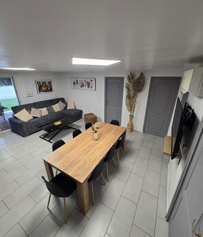 Una sala de estar moderna con una mesa de comedor de madera, sillas negras, un sofá gris y un ventanal grande.