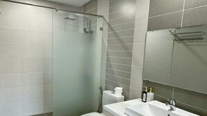 A modern bathroom with a glass-enclosed shower, a white toilet, and a sink with a mirror.