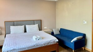 A hotel room with a bed, a blue sofa, and a radiator.