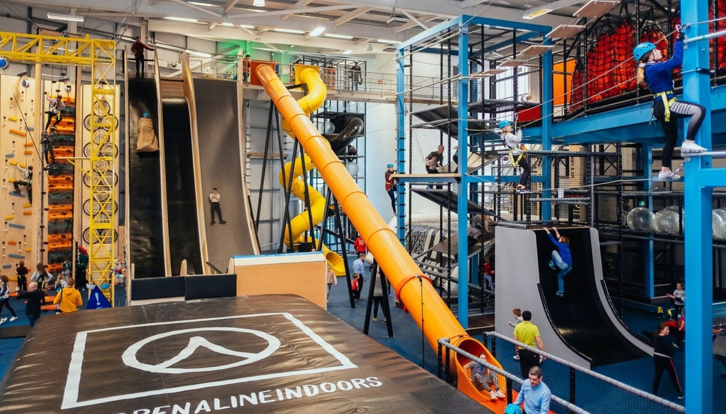 An indoor adventure play area with various climbing structures, slides, and a large yellow slide.
