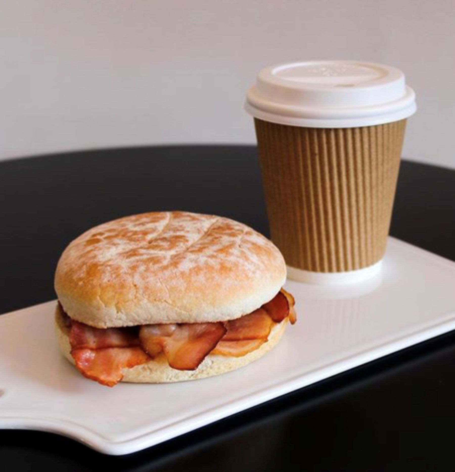 Un sándwich de desayuno con tocino y una taza de café sobre un plato blanco.