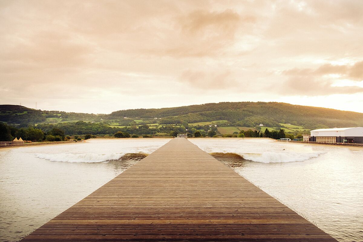 A wooden pier extending into calm water with a hilly landscape in the background.