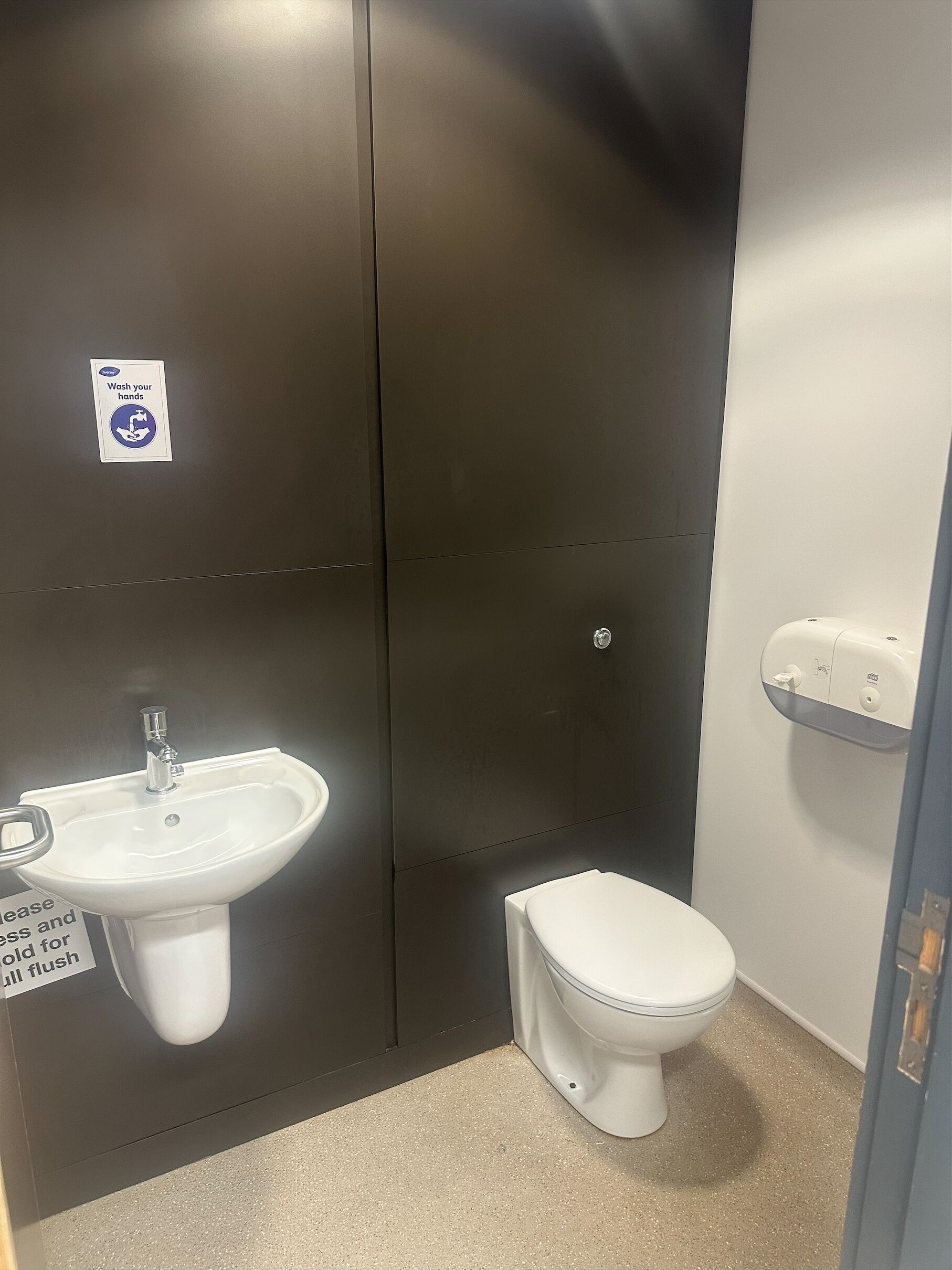 Une petite salle de bain privée équipée d’un lavabo, de toilettes et d’un distributeur de gel hydroalcoolique.
