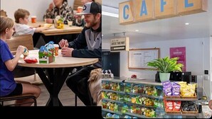 Una cafetería con letreros de madera que deletrean 'CAFE' y un cartel de fila de espera.