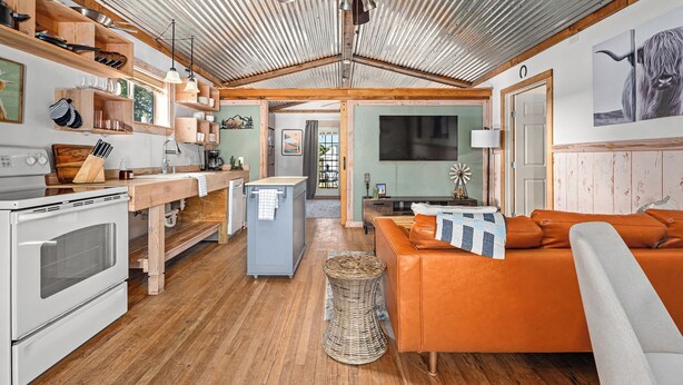 Une cuisine spacieuse avec des étagères en bois, un coin repas et un salon doté d’un canapé.