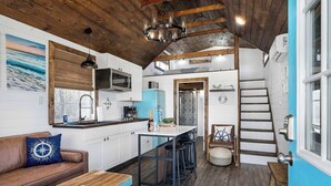 Una cocina compacta con barra, vigas de madera en el techo, una pared azul de acento y una escalera que sube a un nivel superior.