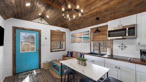 Una cocina con vigas de madera en el techo, una puerta azul, una encimera blanca y un microondas de acero inoxidable.