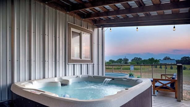Un jacuzzi en una terraza de madera con vistas a un campo y árboles.