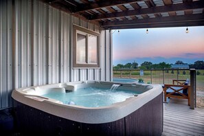Ein Whirlpool auf einer Holzterrasse mit Blick auf ein Feld und Bäume.