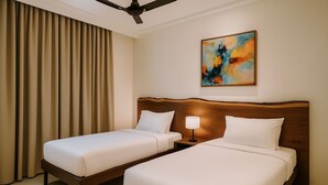 Quarto de hotel com duas camas, um ventilador de teto, um quadro na parede e uma janela com cortinas.