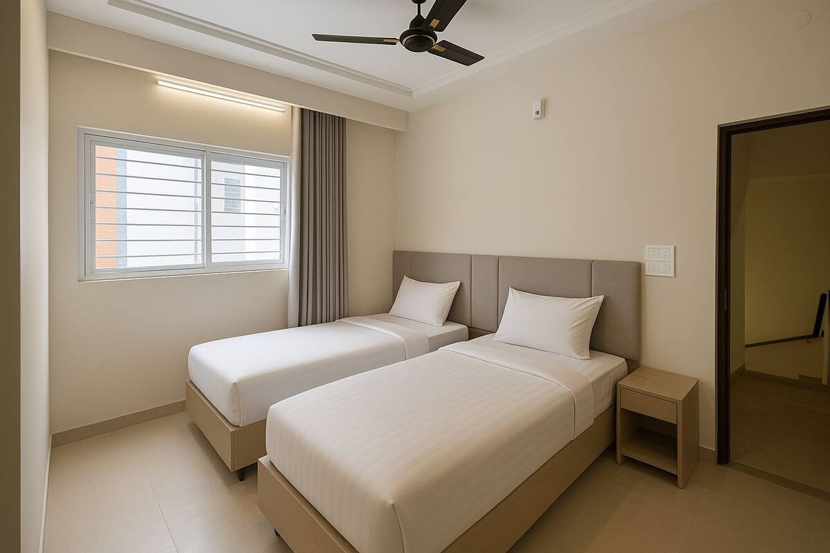 A hotel room with two beds, a ceiling fan, a window with blinds, and a bedside table.