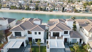A coastal residential area with modern houses featuring tiled roofs and balconies, a beach in the background, and a prominent building with a large archway. - Villa Sarai by Luxury Explorers Collection (Dubai)
