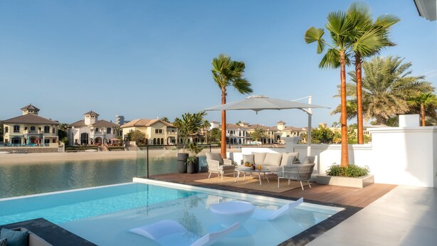 A swimming pool with lounge chairs, a sun umbrella, and a view of a waterfront with buildings. - Villa Sarai by Luxury Explorers Collection (Dubai)