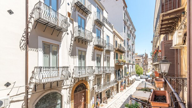 A narrow street with multi-story buildings, balconies with wrought iron railings, and outdoor seating areas. - Giudici Three Bedrooms Apartment by Wonderful Italy (Palermo)