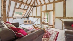 Une pièce au style rustique, avec des poutres apparentes, une table basse en verre, des canapés en cuir et un tapis rouge à motifs.