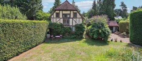A traditional half-timbered house with a well-maintained garden, a hedge, and a small patio area.