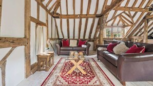 Un intérieur rustique avec des poutres apparentes, un canapé en cuir marron, un tapis à motifs rouges et une table basse en bois.