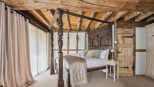 Un lit à baldaquin dans une chambre rustique avec des poutres apparentes, une armoire en bois et une fenêtre avec des rideaux.
