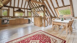 Une cuisine rustique avec des poutres en bois, une table à manger et un tapis rouge à motifs.