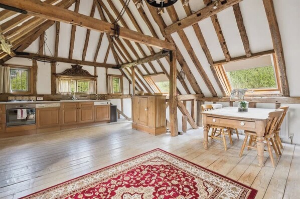 A rustic kitchen with wooden beams, a dining table, and a red patterned rug.
