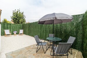 Un patio al aire libre con una mesa redonda y cuatro sillas, un par de sillones de descanso y un toldo grande.