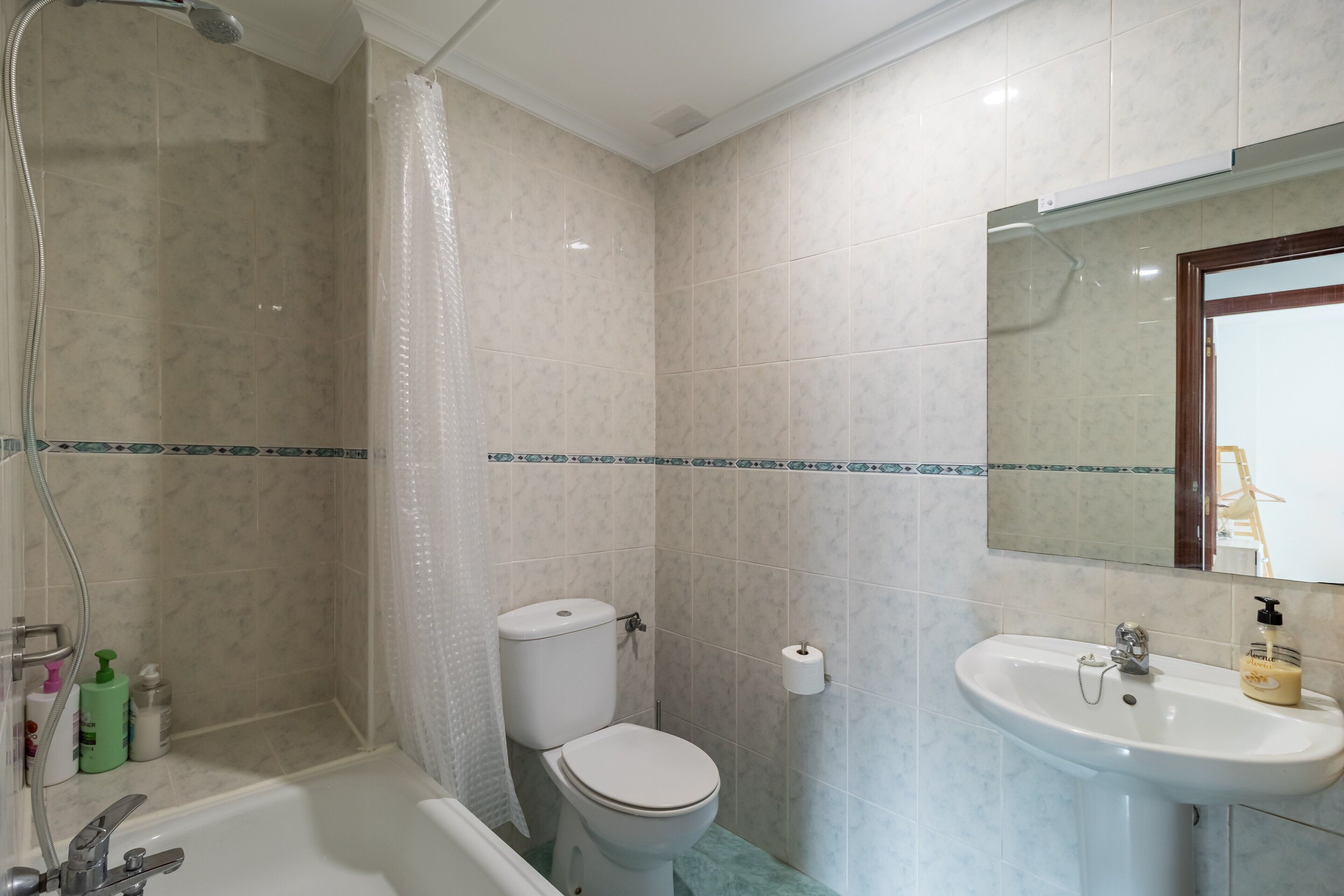 Een badkamer met douche, toilet, wastafel en spiegel.