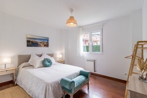 Un dormitorio con cama, lámparas de noche, una lámpara colgante, una ventana con vistas y un radiador.