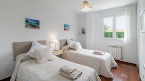 A hotel room with two beds, a window, a radiator, and a hanging light fixture. - Ground Floor Apartment with Garden 'Costa Quebrada' (Liencres)