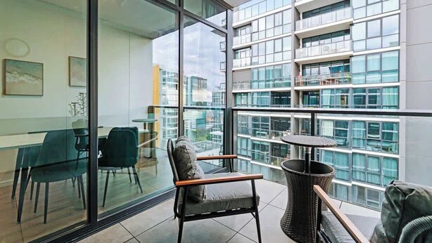 A modern interior with a glass partition, a dining area with chairs, a small table, and a view of a high-rise building.