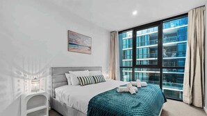 Un dormitorio moderno con un ventanal grande, una cama con una manta color turquesa y una mesita de noche con una lámpara.