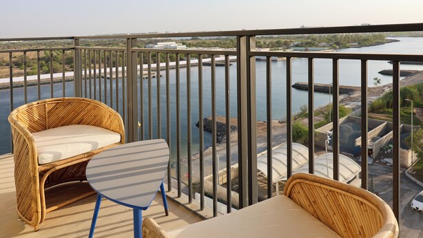 Een balkon met rieten meubels, een tafel en uitzicht op een rivier en verre gebouwen.