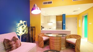 Een moderne woonkamer met een bank, twee rieten fauteuils, een salontafel, en een keuken op de achtergrond.