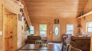 A wooden cabin interior with a dining table, two sofas, and a door with a window.
