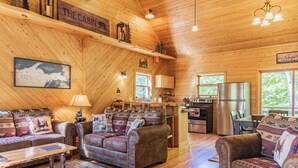 A cabin interior with a wooden interior, a dining area, kitchen, and a living room with two sofas and a coffee table.