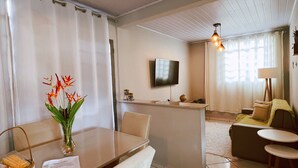 A modern hotel room with a dining area, a sofa, a TV, and a window with curtains.