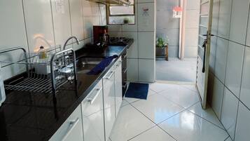 Uma cozinha com paredes de azulejos brancos, bancada preta e pia de aço inoxidável.
