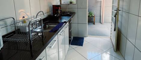 A kitchen with white tiled walls, a black countertop, and a stainless steel sink.