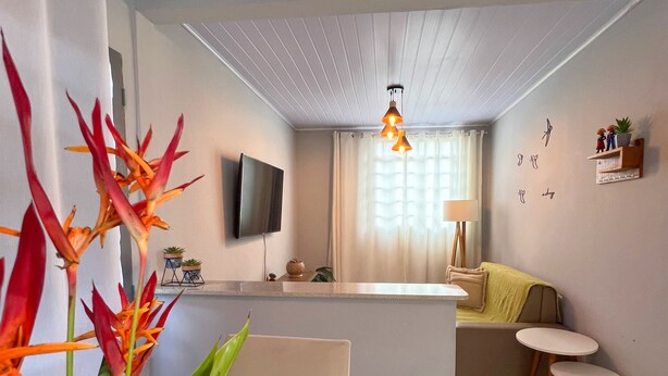 A modern living room with a flat-screen TV, a dining table, and a kitchen area with a counter.