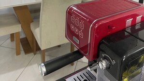 Een eethoek met een tafel, stoelen en een rood apparaat, mogelijk een koffiezetapparaat, in een moderne ruimte met een televisie aan de muur.