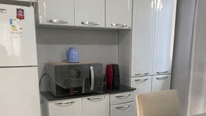 Een compacte keuken met witte kastjes, een magnetron, waterkoker en koffiezetapparaat.