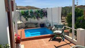 Ein kleiner Poolbereich im Freien mit einem Stuhl und Tisch, umgeben von einem weißen Zaun und Pflanzen.