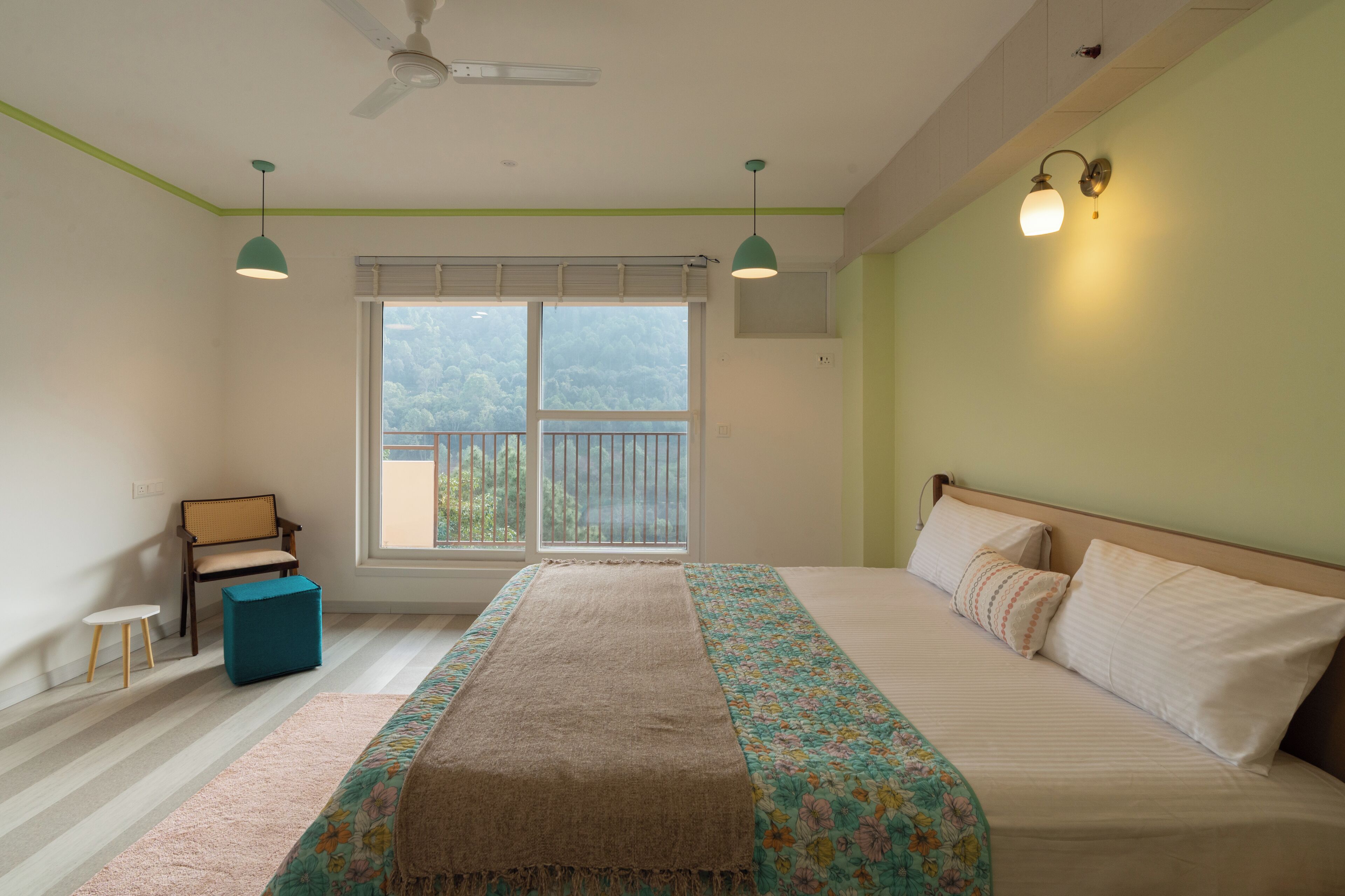 Quarto com cama, janela, ventilador de teto, mesinha e cadeira.